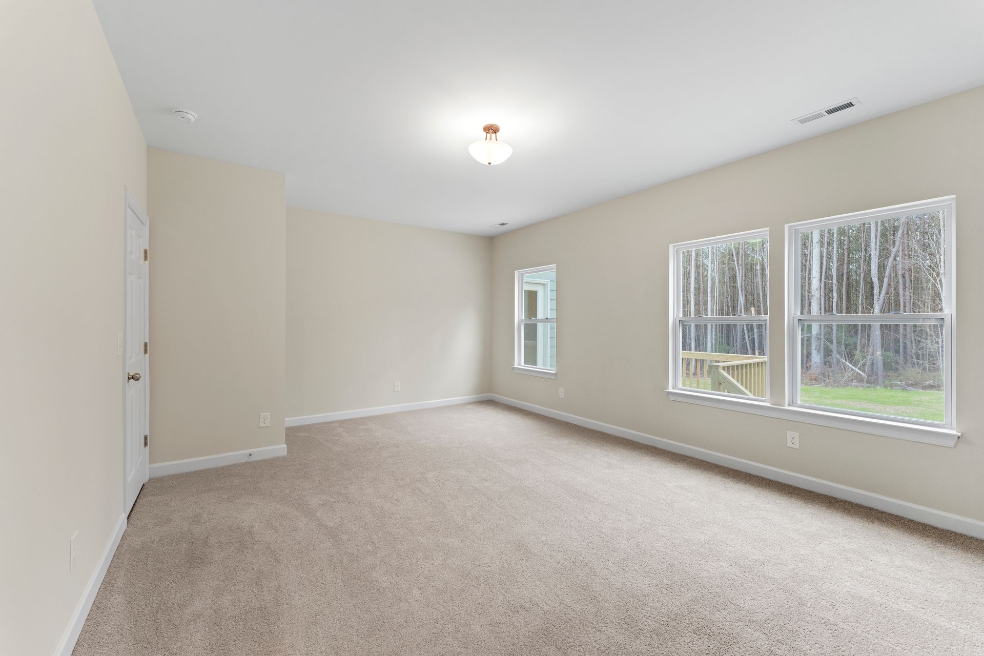 An empty room with a carpeted floor and two windows.