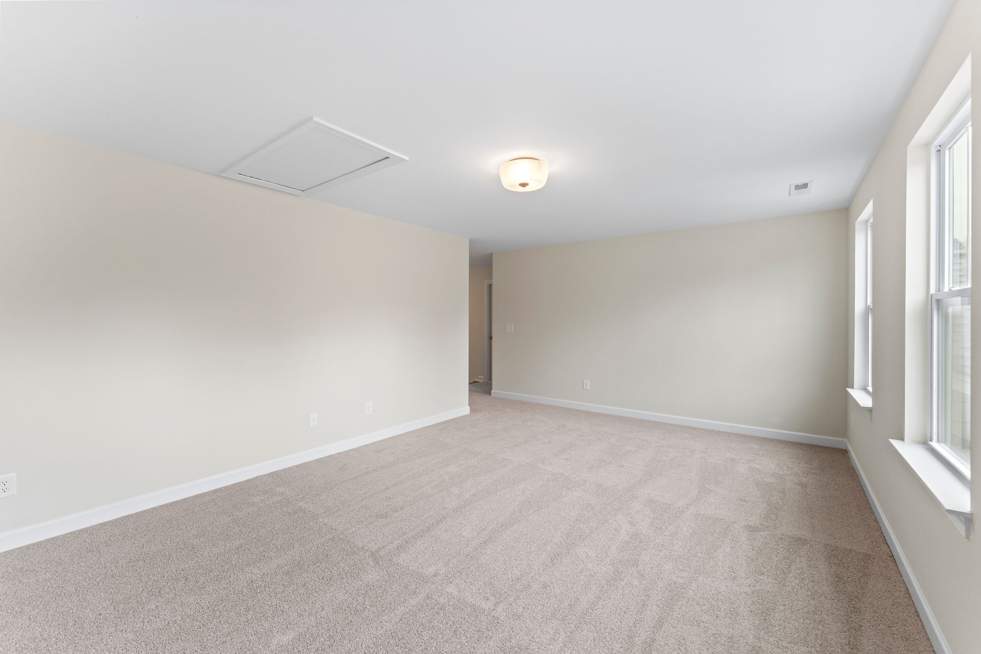 An empty room with a carpeted floor , white walls , and two windows.