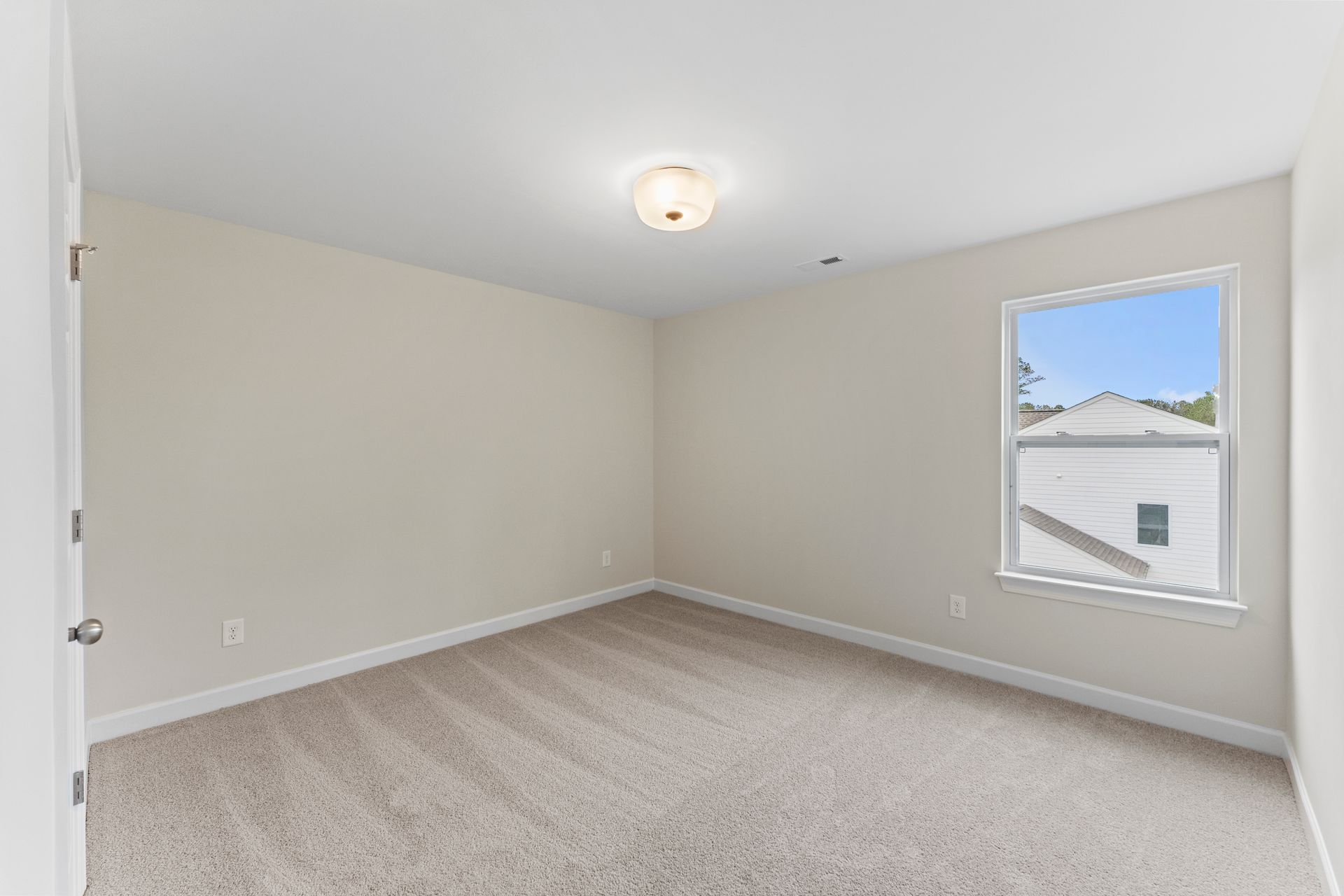 An empty bedroom with a window and a carpeted floor.