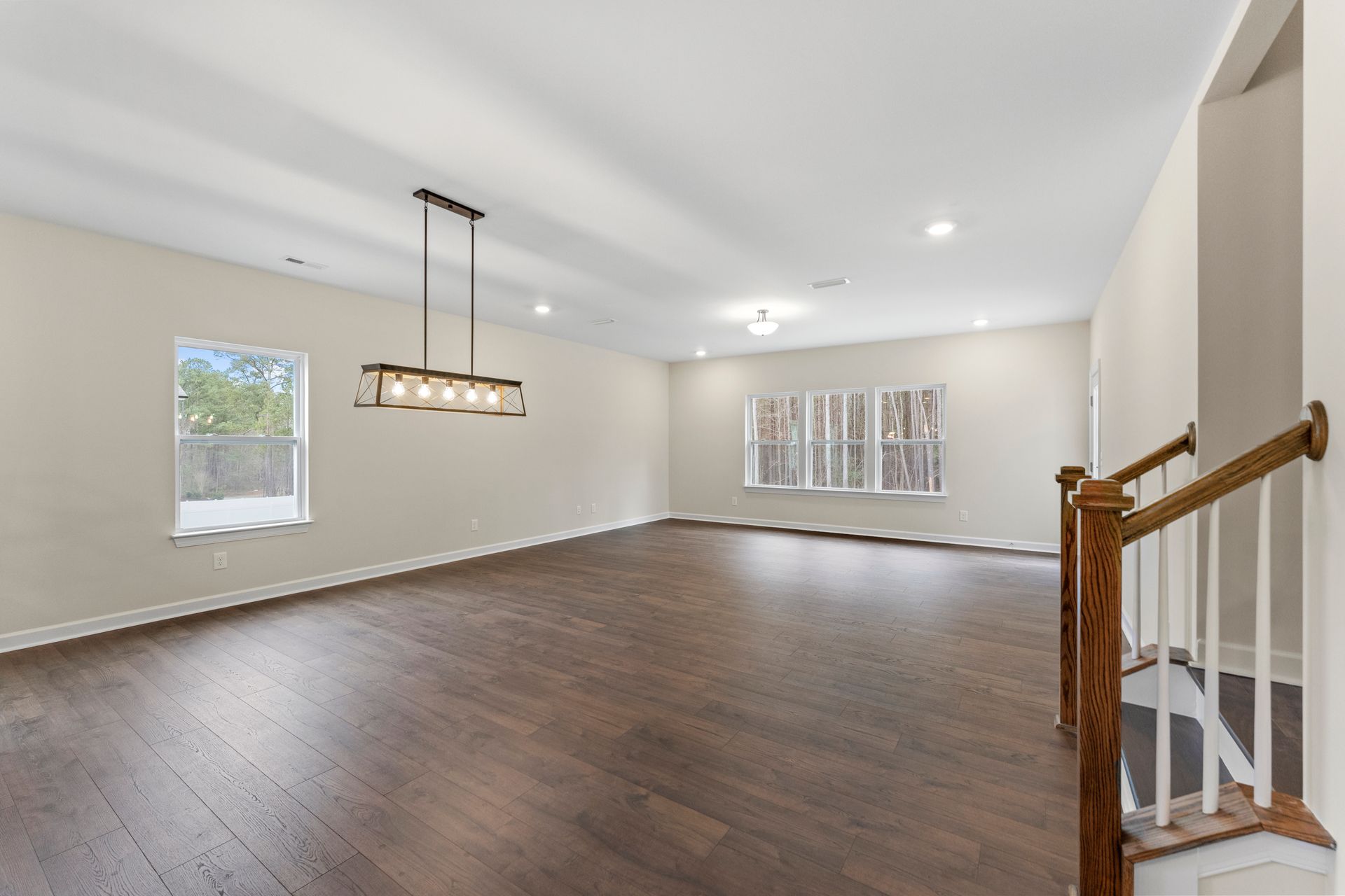 An empty living room with hardwood floors and stairs leading to the dining room.