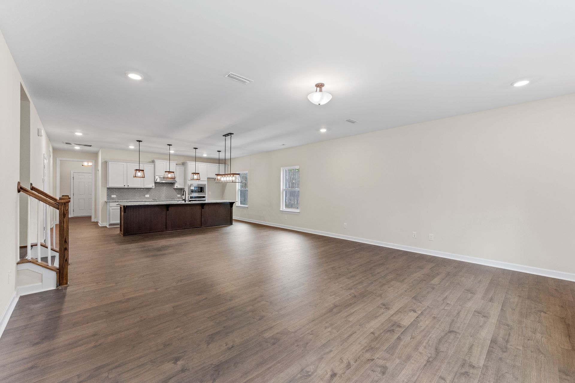 An empty living room with hardwood floors and a kitchen in the background.