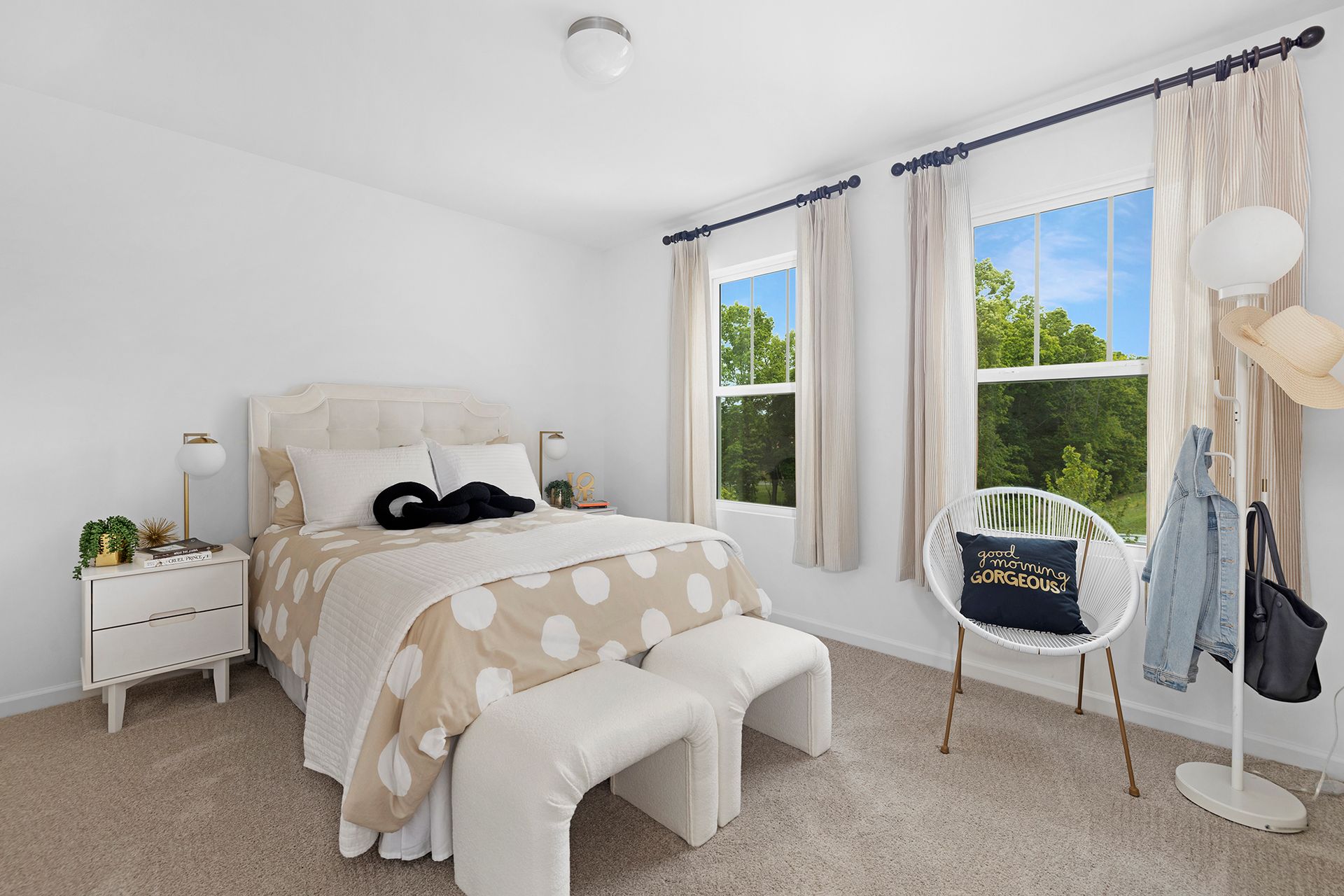 A bedroom with a bed , chair , nightstand and two windows.
