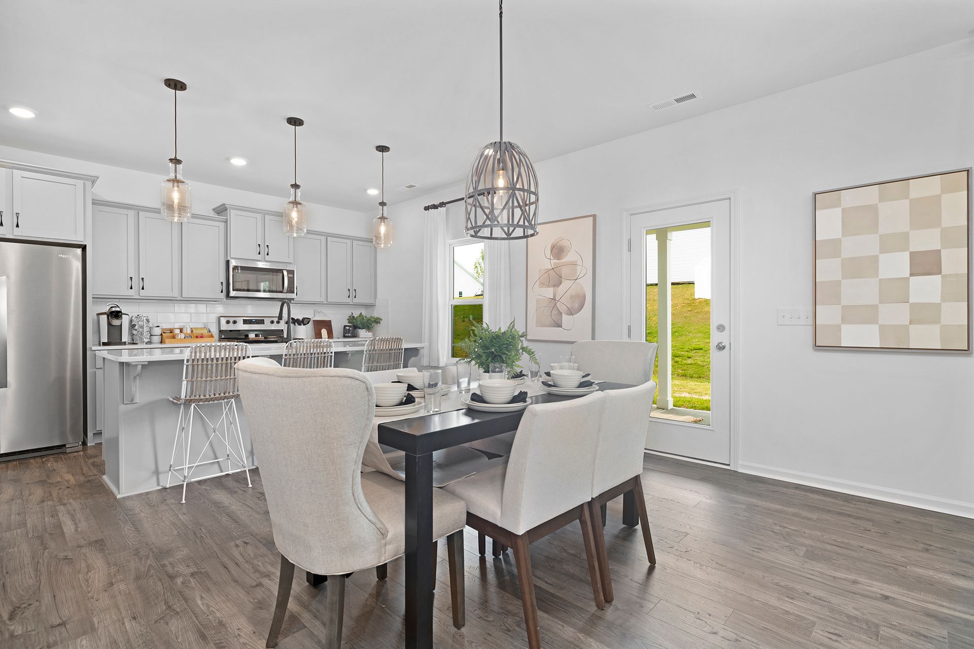 A dining room with a table and chairs and a kitchen in the background.