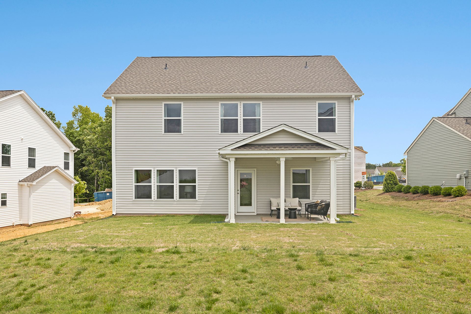 The back of a house with a porch and a large lawn in front of it.
