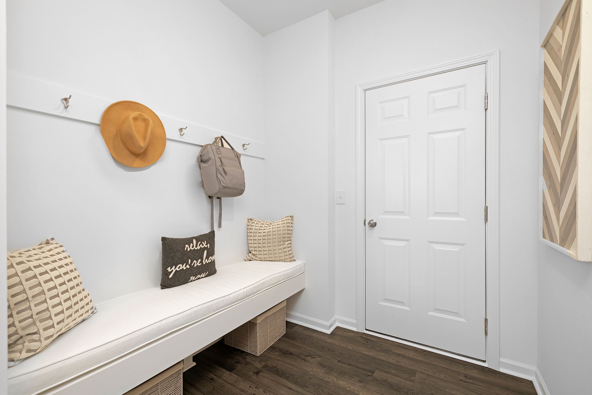 There is a bench in the middle of the room with a hat hanging on the wall.