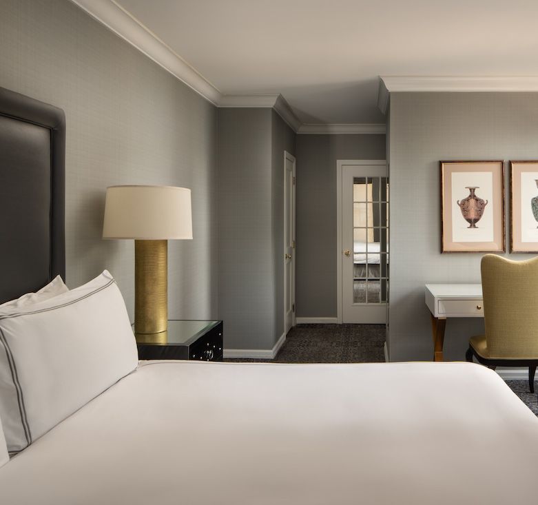 Bedroom with a white bed, gold lamp, white desk, and two framed prints on the wall.
