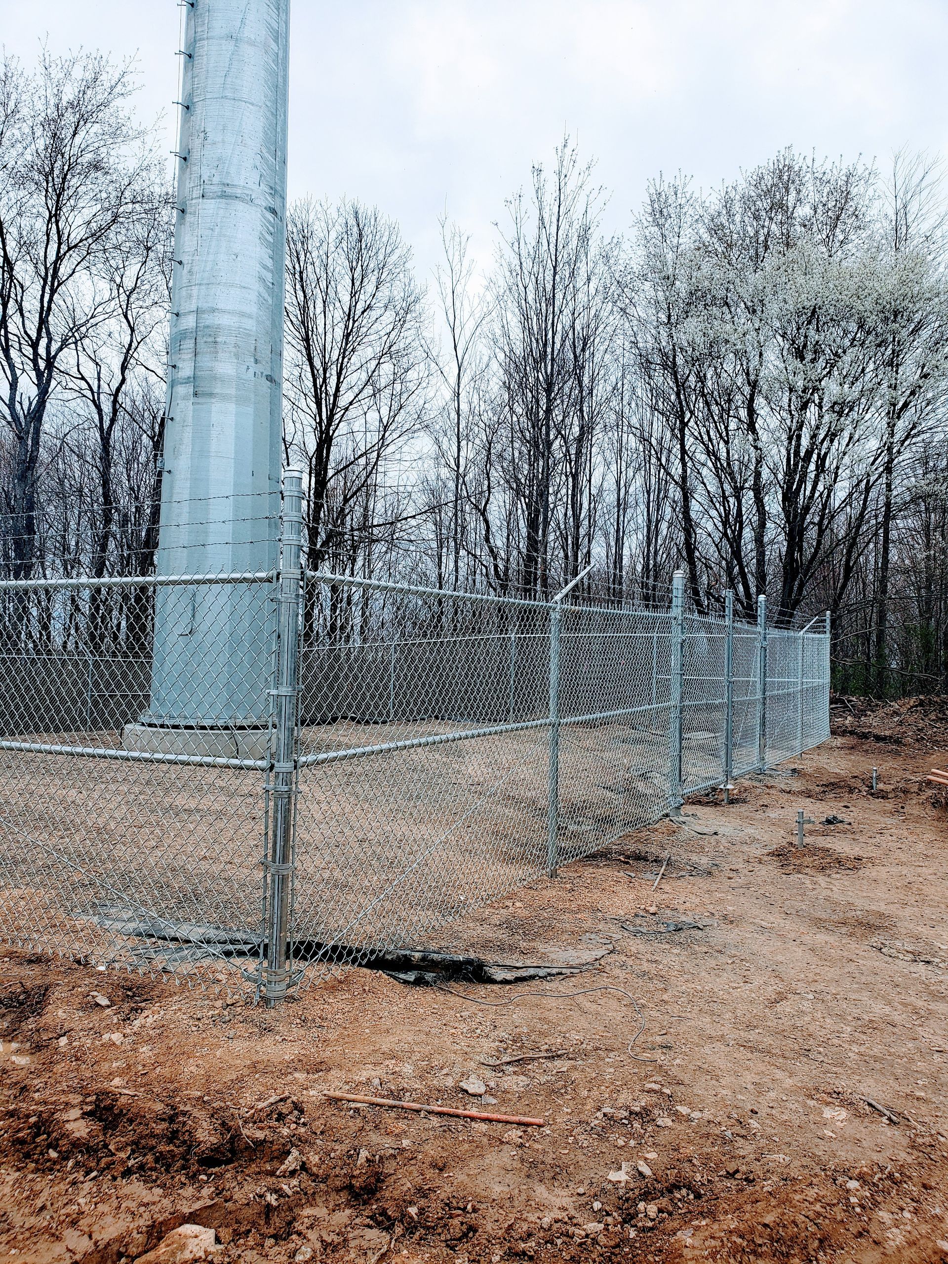 A tall, metal communications tower surrounded by a chain-link fence in a wooded area.