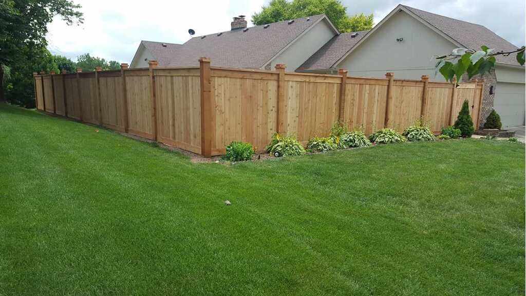 Wooden fence surrounds a grassy backyard near a house