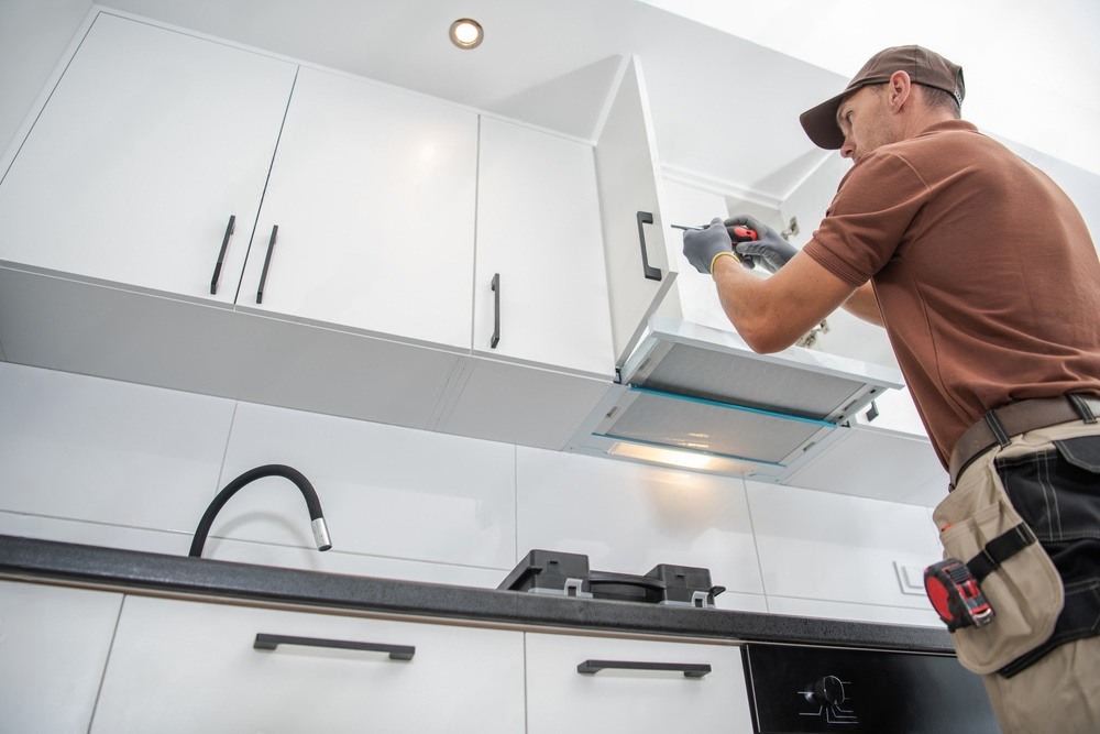 a man is installing a hood in a kitchen .