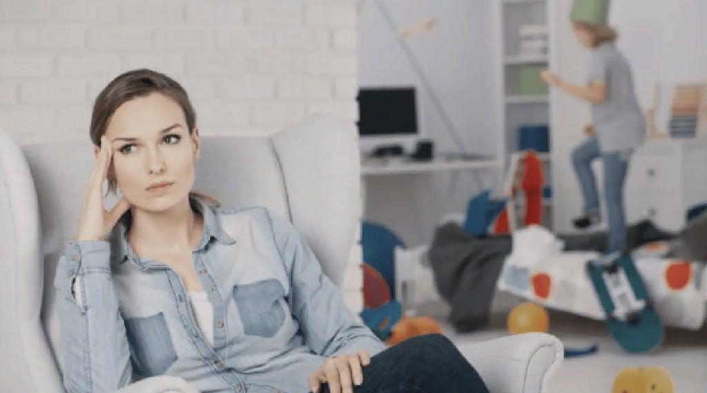 A woman is sitting in a chair in front of a messy room.