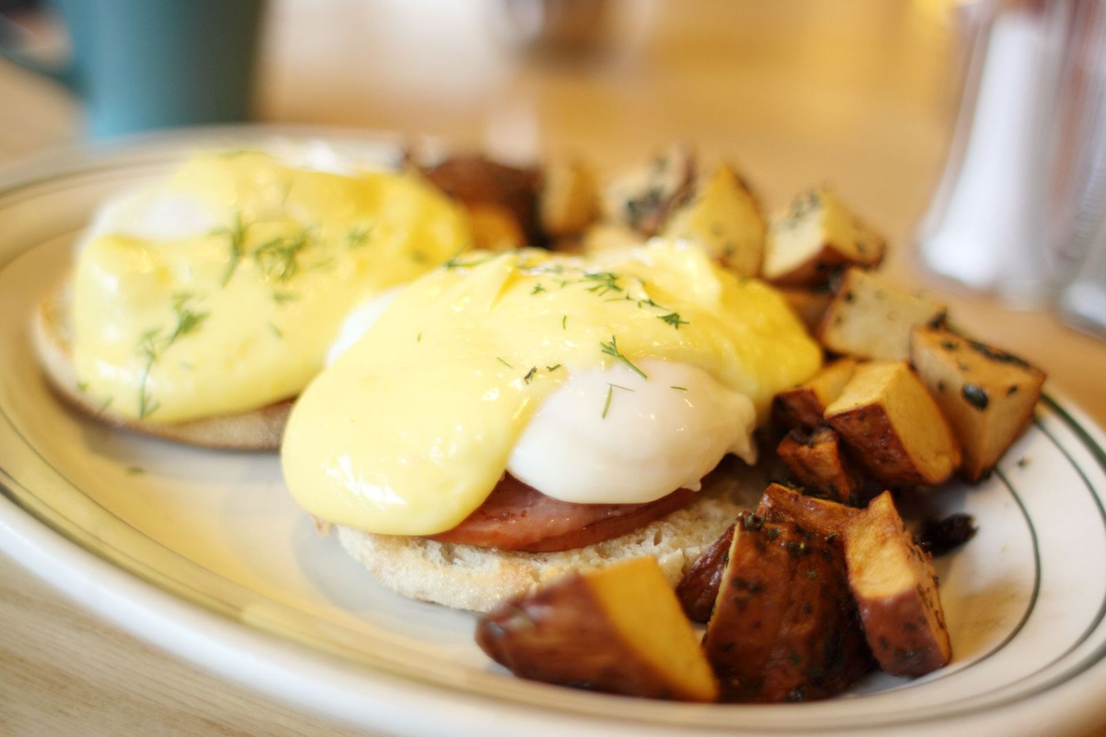 Eggs Benedict with hollandaise sauce and seasoned potato wedges on a white plate