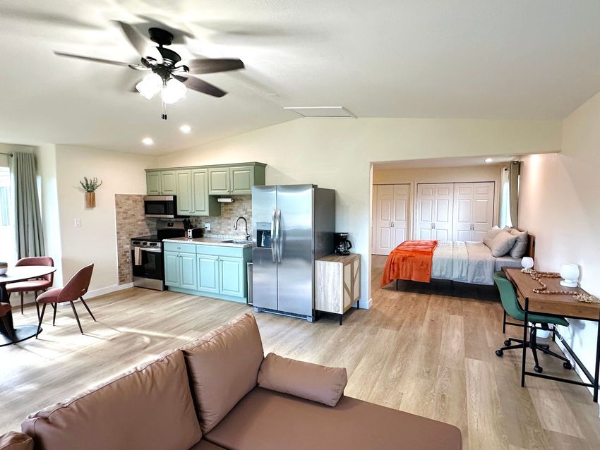 Open-concept living room with kitchen, gray couch, and a bedroom nook in the back