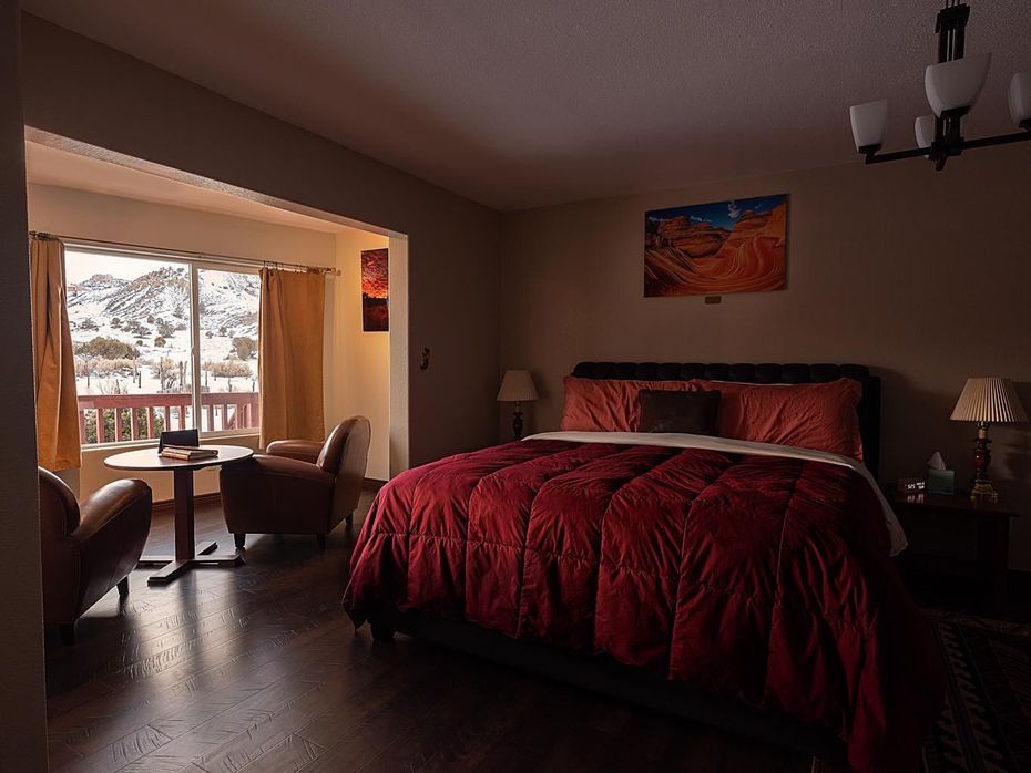 Cozy bedroom with a red bedspread, sitting area, and snowy mountain view through large sliding doors