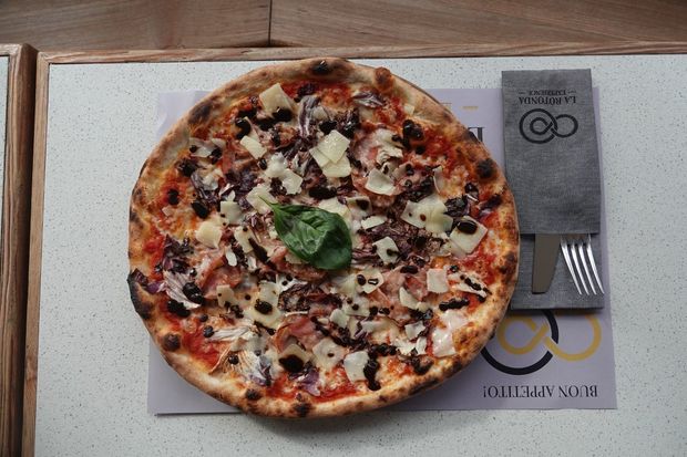 Pizza su un piatto con una piccola guarnizione verde, servita su una tovaglietta con una forchetta accanto.