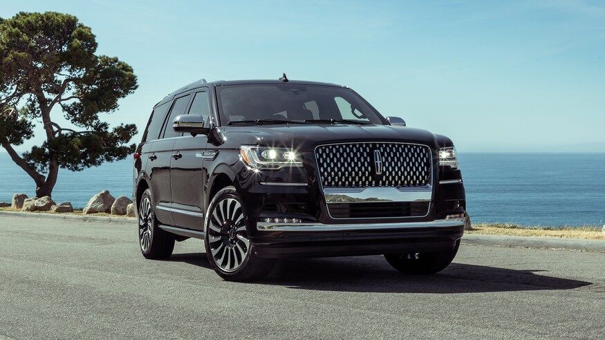a black lincoln navigator is parked on the side of the road near the ocean .