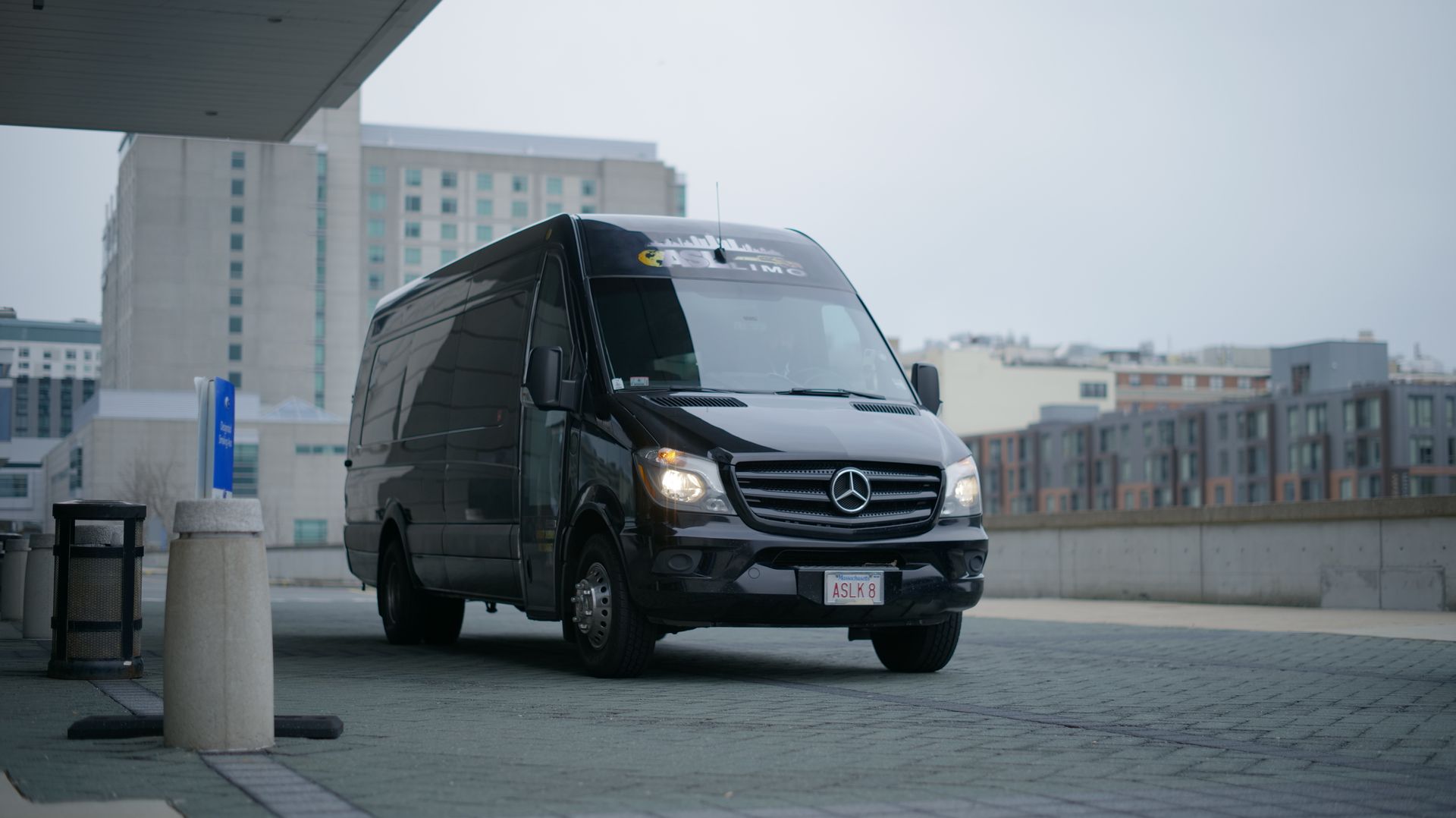 a black sprinter van is parked in a parking lot in front of a building .