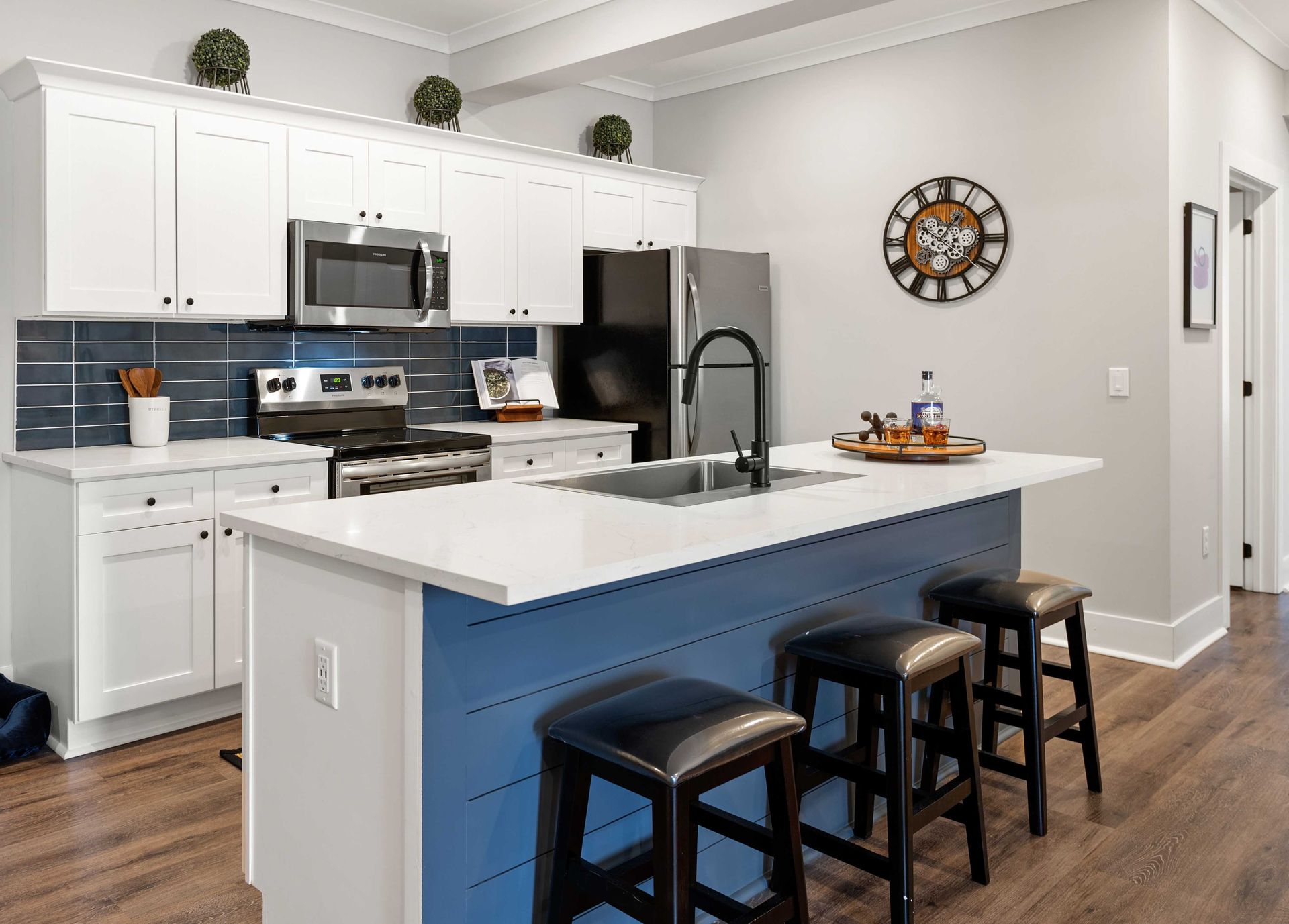 Apartment kitchen with white cabinets, a blue island, stools, a refrigerator and a clock on the wall.