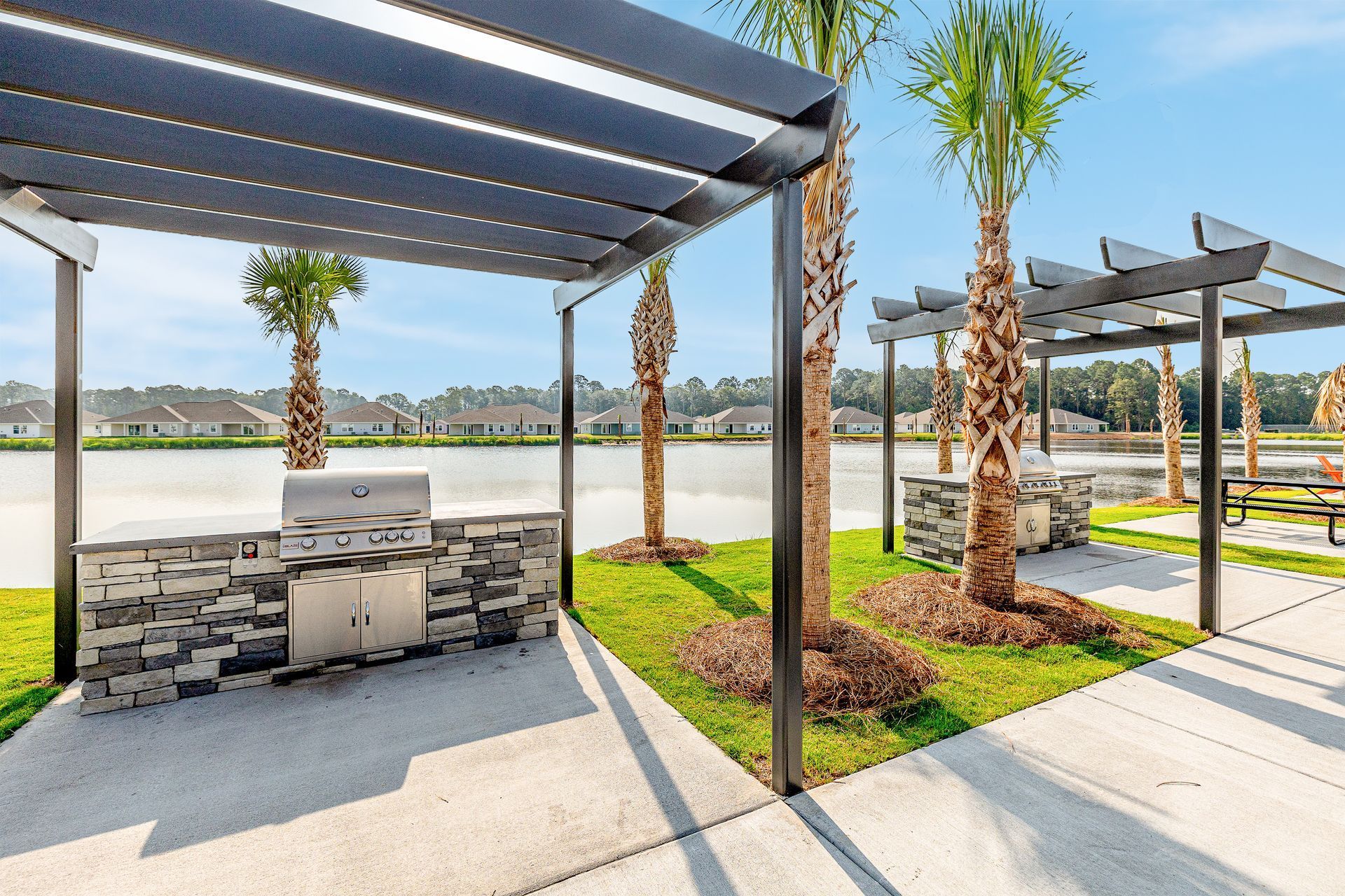 A grill is sitting under a pergola next to a lake at Pointe Grand Brunswick in Brunswick, GA.