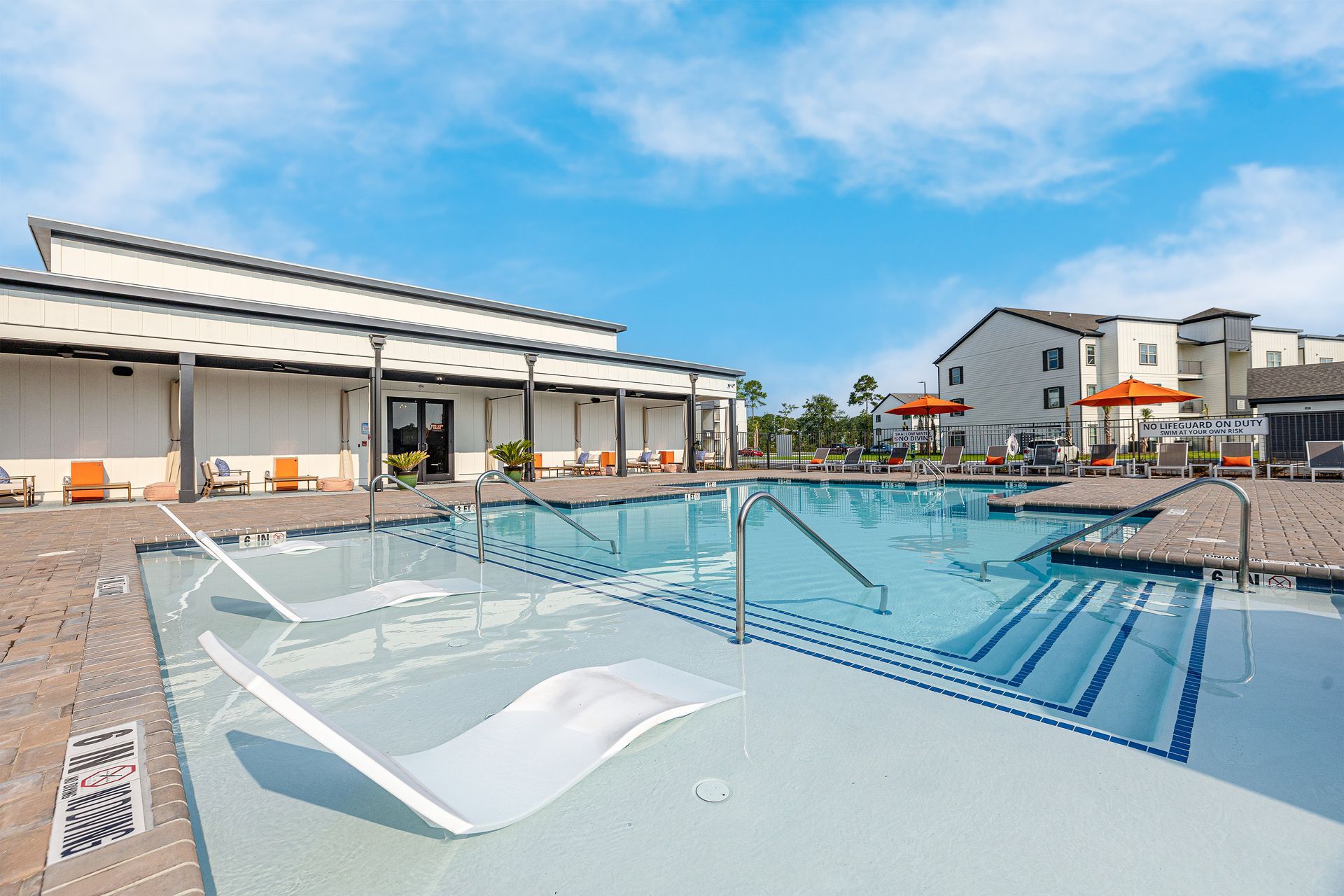 A large swimming pool surrounded by chairs and umbrellas in front of a building at Pointe Grand Brunswick in Brunswick, GA.