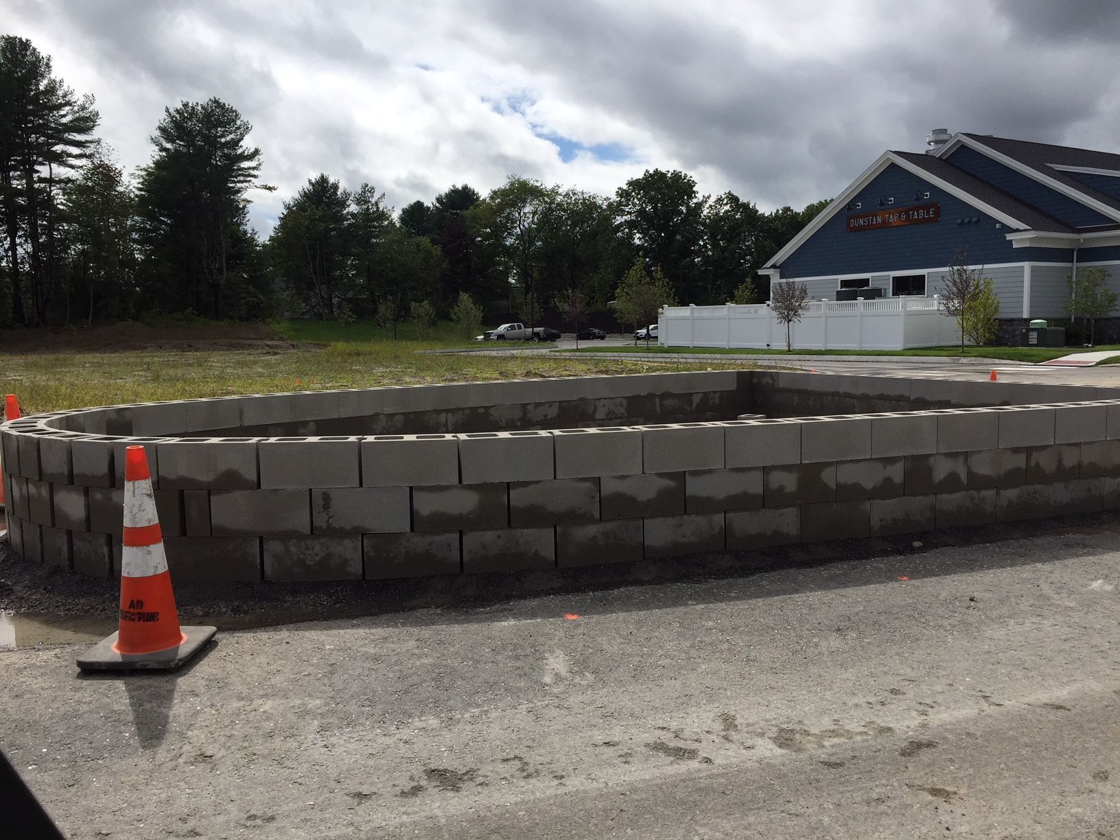 A low, curved concrete block wall under construction, with a traffic cone in the foreground.