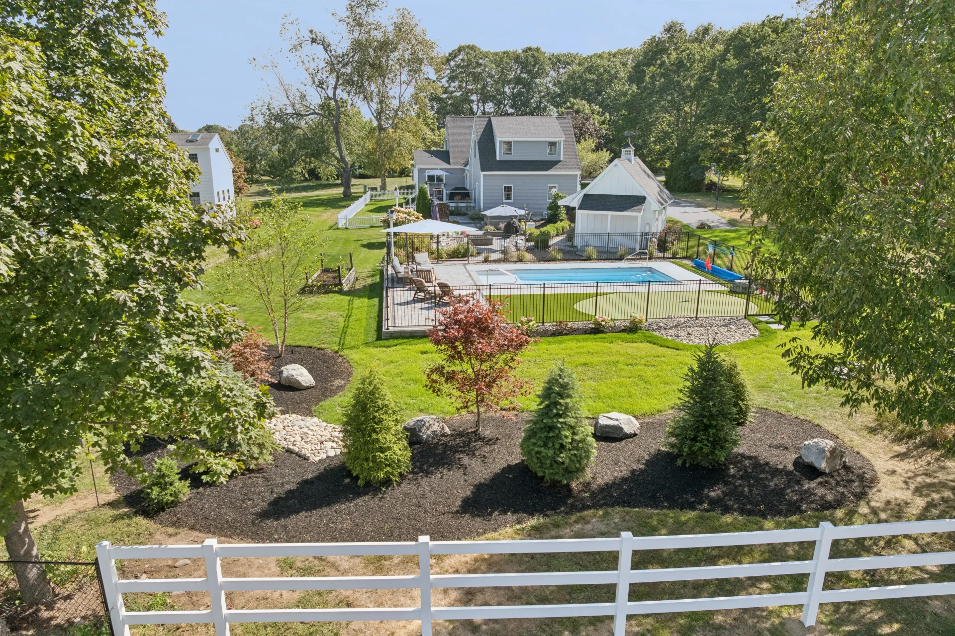 Large house with a pool and fenced-in yard, surrounded by trees.