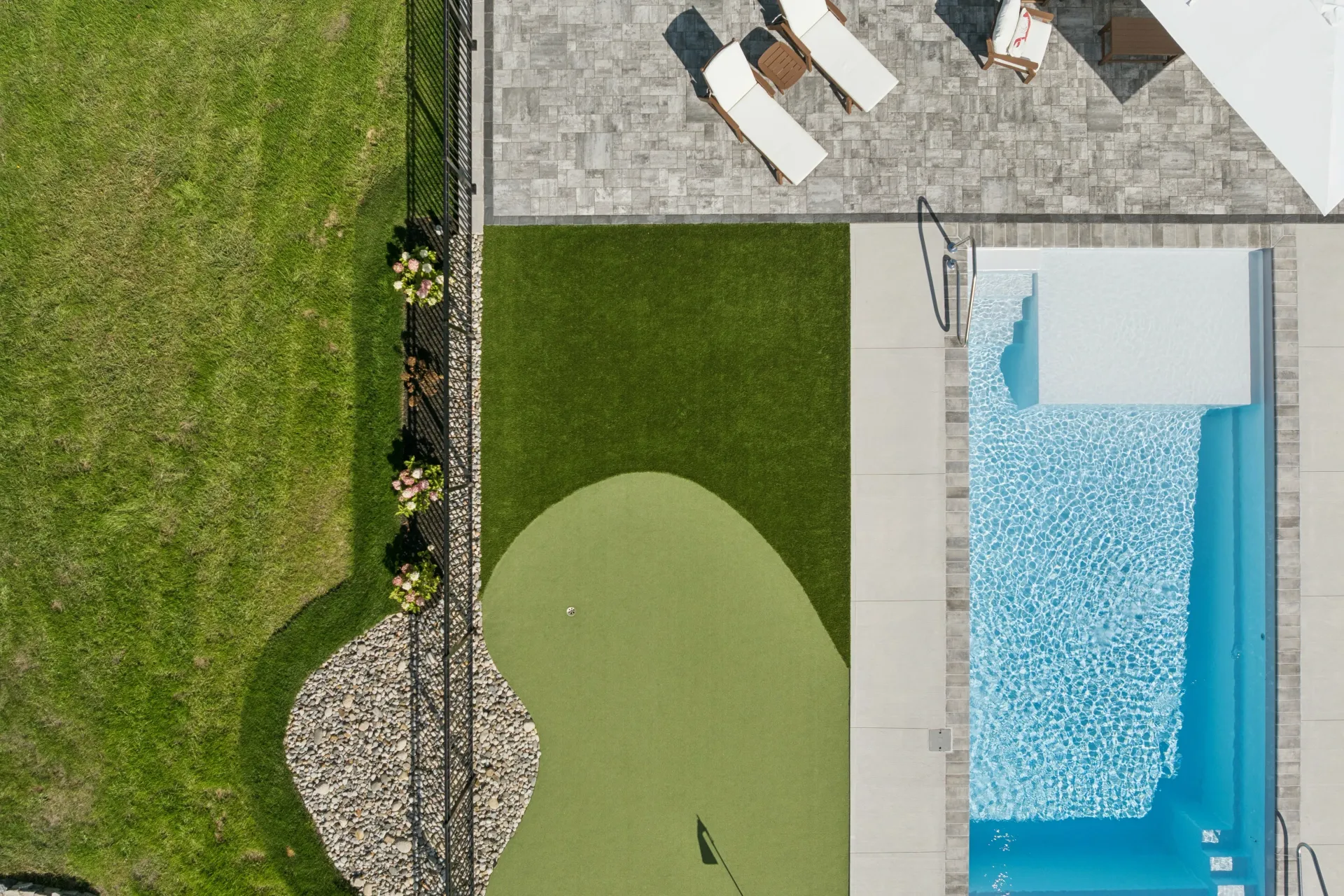 Aerial view: swimming pool, putting green, patio with lounge chairs, and grassy lawn.