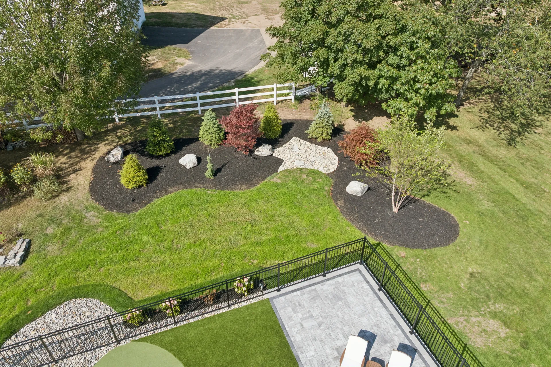 Overhead view of landscaped yard with mulch beds, shrubs, and a patio with lawn furniture.