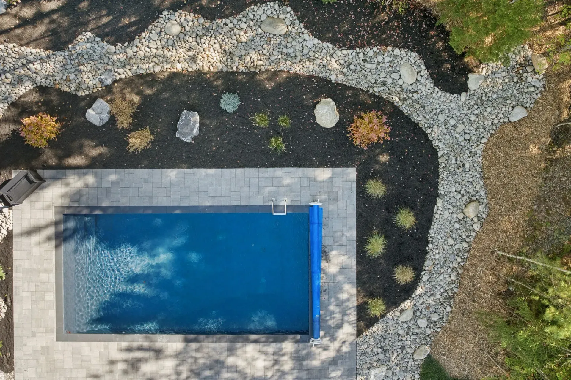 Aerial view of a rectangular pool with blue water surrounded by landscaping, rocks, and mulch.