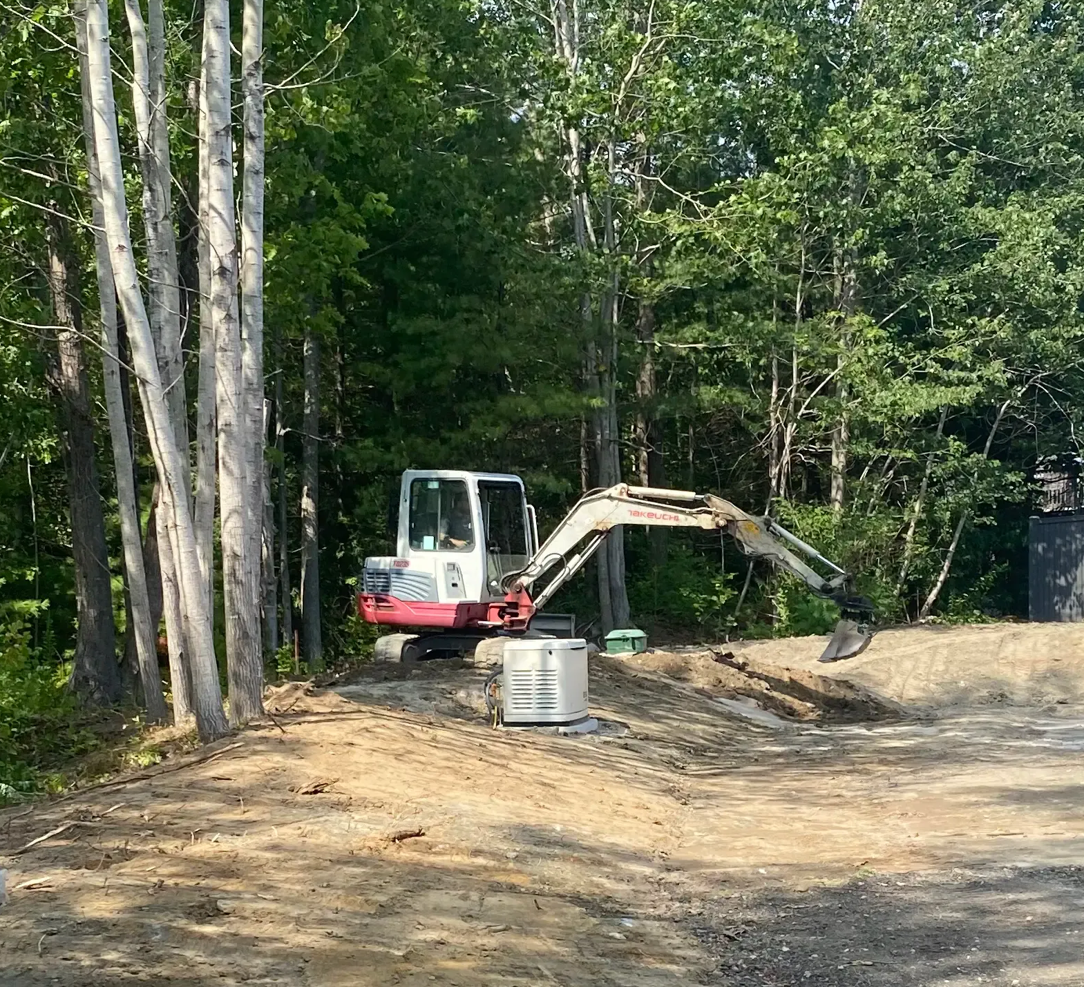 Small excavator on a dirt mound near trees, with a generator nearby.