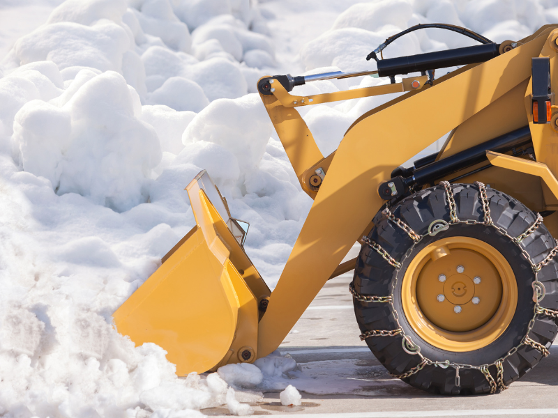 Yellow snowplow with chains on tires pushing snow.