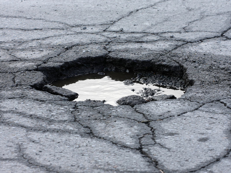 Large pothole filled with water in cracked asphalt.