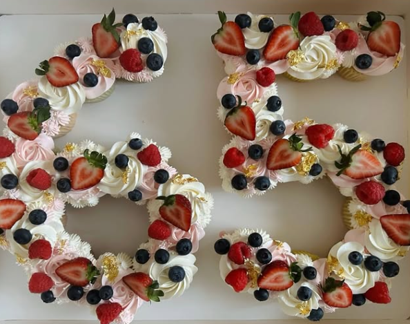 Cupcake arrangement shaped as the number 65, decorated with pink frosting, fresh berries, and gold leaf.