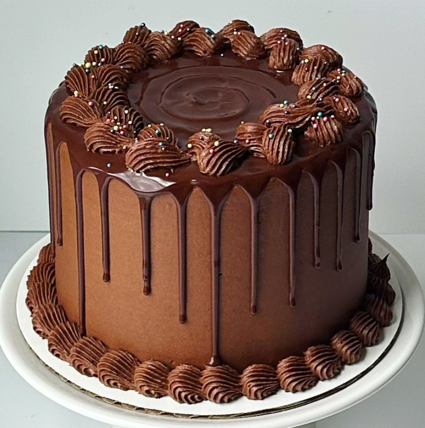 Chocolate cake with dripping frosting, piped frosting on top and bottom, and sprinkles.