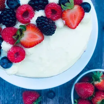 White frosted cake topped with fresh berries on a white plate; a bowl of strawberries beside it.