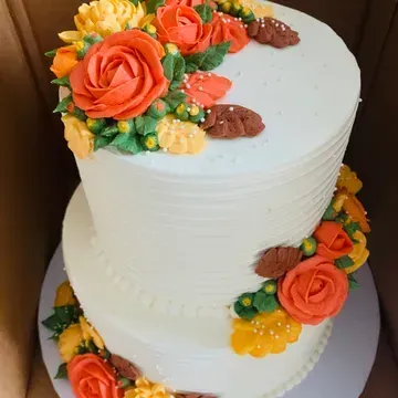Two-tiered white cake with buttercream frosting, decorated with orange, yellow, and brown floral arrangements.