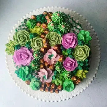 A beautifully decorated cake, resembling a succulent garden with green, pink, and brown buttercream frosting.