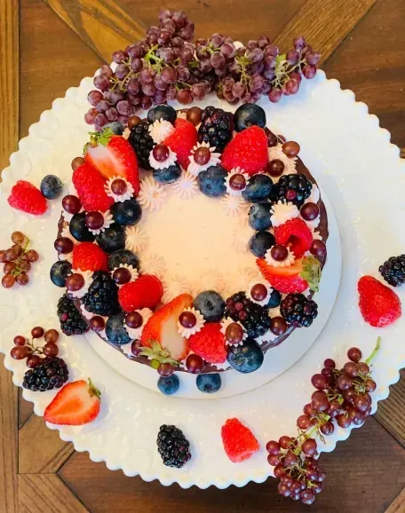 A round cake decorated with strawberries, blueberries, blackberries, and grapes on a white plate.