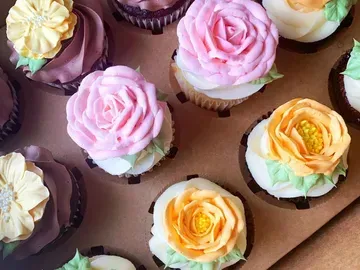 Cupcakes in a box with colorful buttercream flower decorations, including pink, yellow, and orange roses.