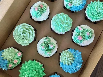 Box of frosted cupcakes decorated to resemble succulents, in shades of green, blue, and white.