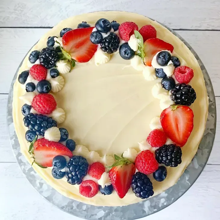 A round cake frosted in white, topped with a ring of fresh berries: strawberries, blueberries, raspberries, and blackberries.