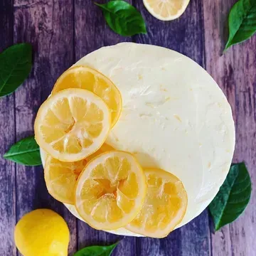 Lemon cheesecake decorated with candied lemon slices and fresh green leaves on a dark wooden surface.