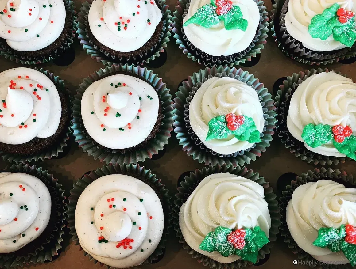 Close-up of a dozen cupcakes in a box, topped with white frosting and Christmas decorations.