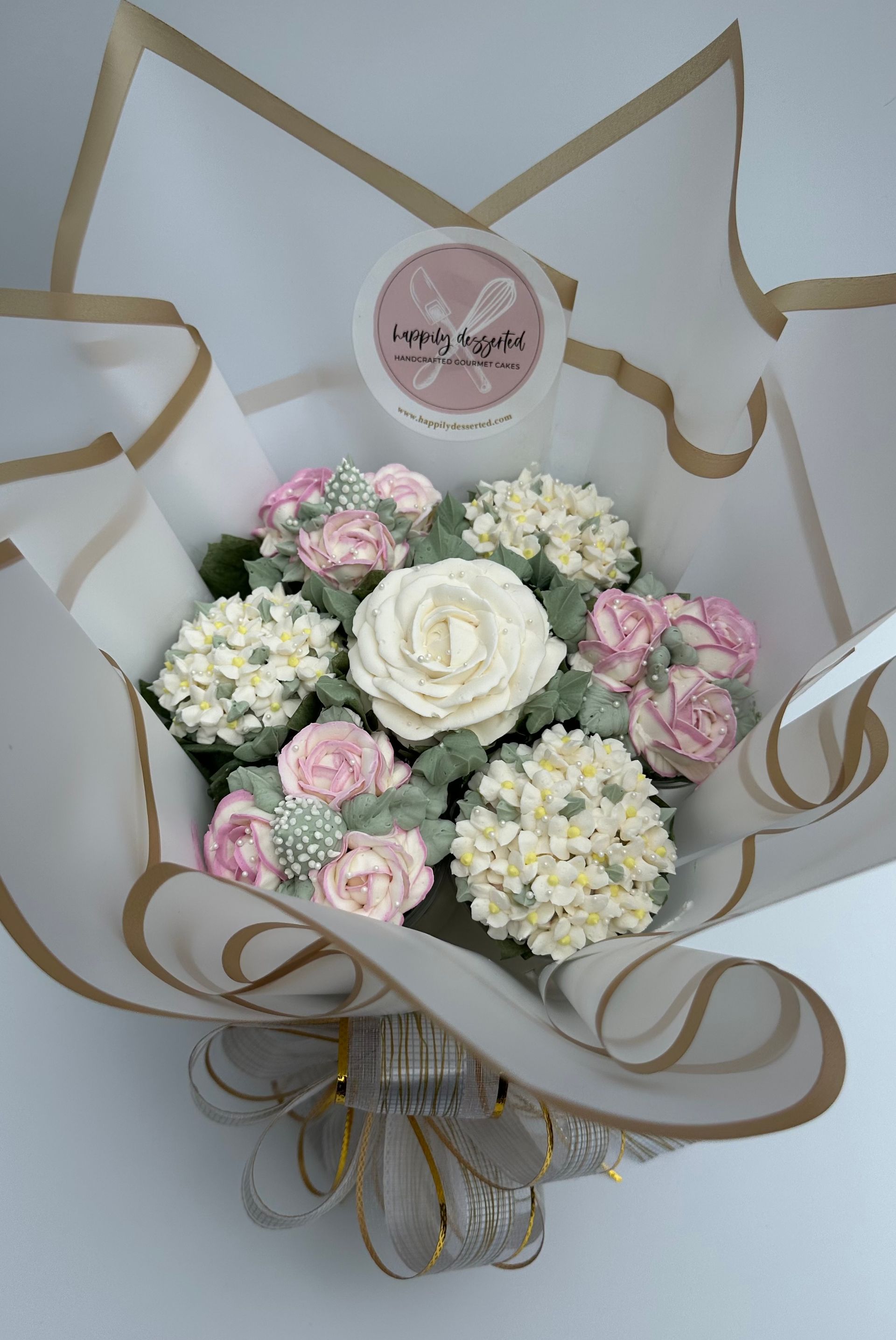 A bouquet of decorated cupcakes arranged to resemble flowers in white and pink, wrapped in decorative paper.