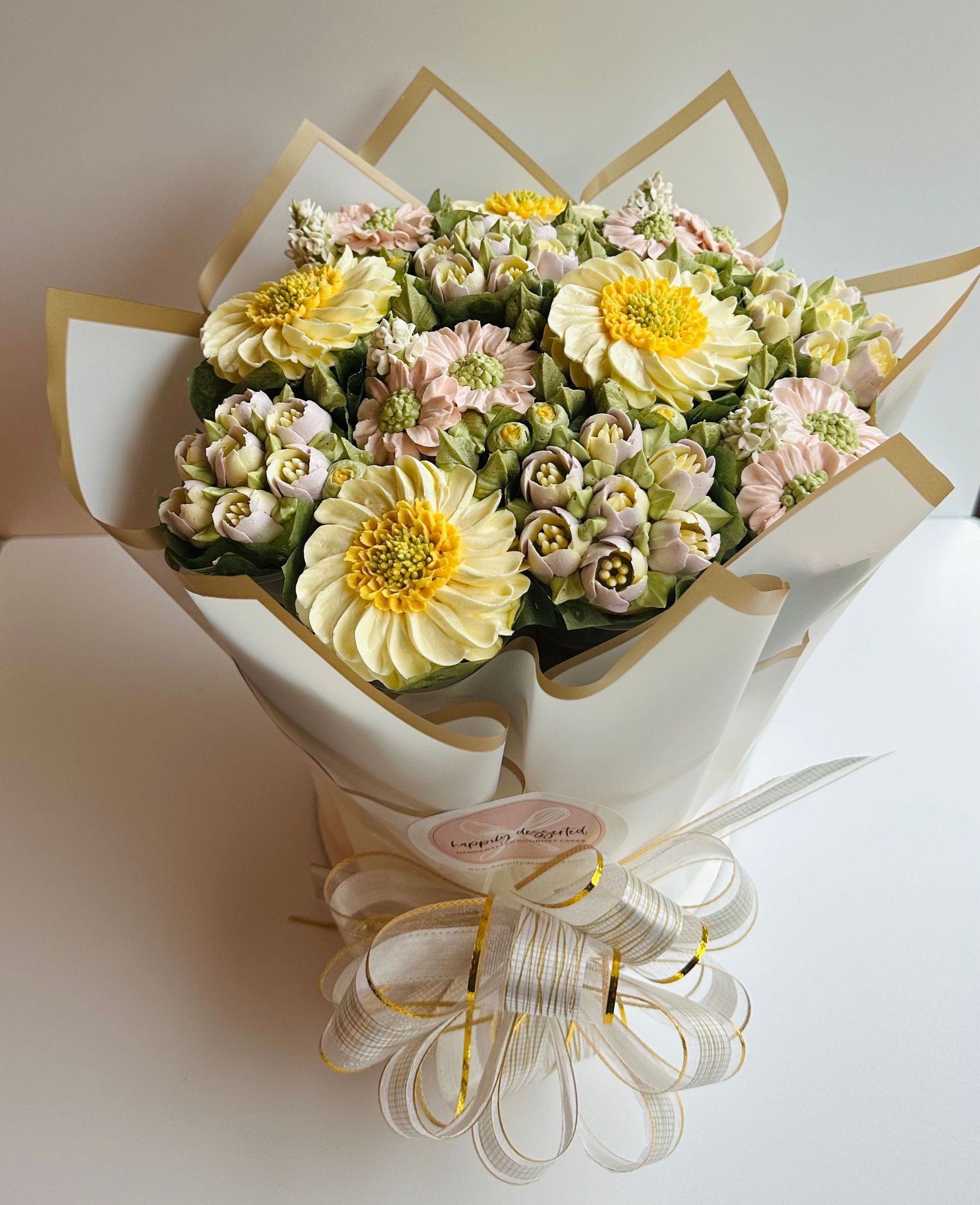 A bouquet of buttercream flowers, including yellow daisies and pink blooms, wrapped in white paper and tied with a ribbon.