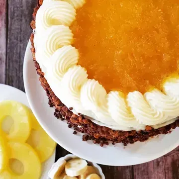 Pineapple upside-down cake on a white plate, with a pineapple and banana garnish. It has white frosting swirls and a brown crust.