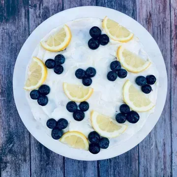 Lemon cake with white frosting, decorated with blueberries and lemon slices, on a white plate.