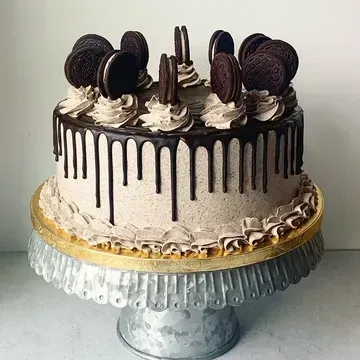 Oreo cake on a silver cake stand, with chocolate frosting, drip detail, and cookies on top.