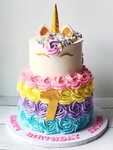 Two-tiered unicorn birthday cake with rainbow frosting and a golden horn, celebrating a 7th birthday.