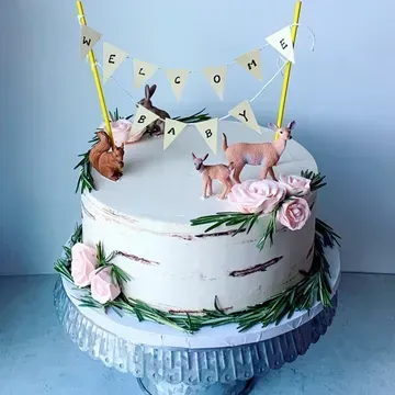 Baby shower cake with rustic design, adorned with toy animals, pink flowers, rosemary sprigs, and a
