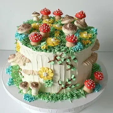 A two-tiered cake decorated as a whimsical forest scene. It features buttercream